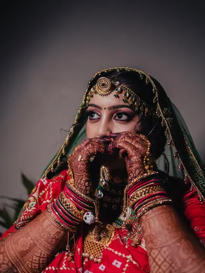 A beautiful and shy portrait of the bride adjusting her veil, her mehndi-covered hands framing her face.