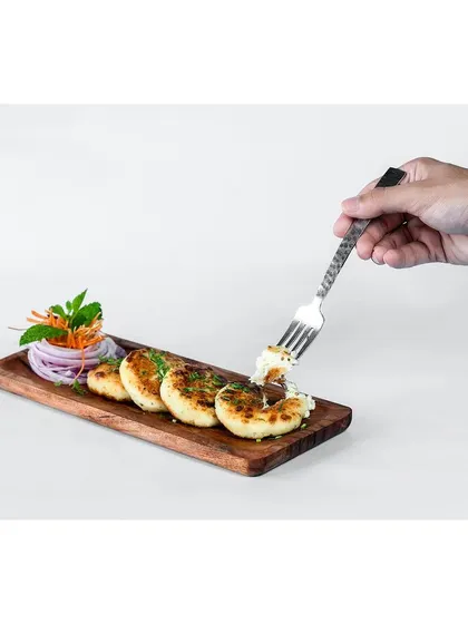 Dahi ke kebab on a wooden serving board, with a hand using a fork to show the soft interior. This highlights the product's key attribute, its creamy texture.