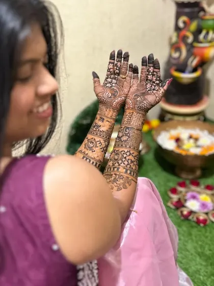 A candid shot of a bride-to-be admiring her intricate mehendi. The design features detailed work on both the front and back of her hands.