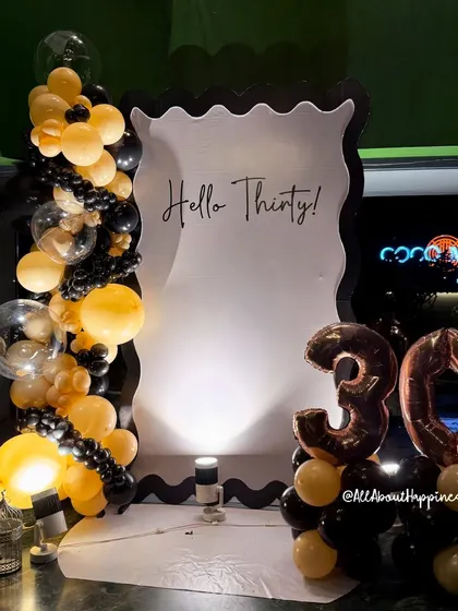 "Hello Thirty!" This stylish black and gold decor is perfect for a 30th birthday party. The custom-shaped backdrop and balloon arrangement create a chic and modern photo opportunity.