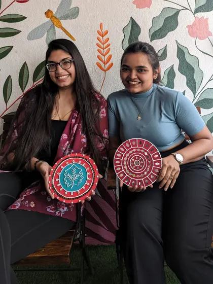 Two friends with their finished Lippan art pieces, each with a unique and colorful design.