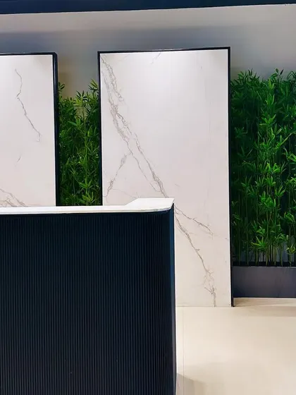 The reception desk at the ALP Overseas Experience Center is framed by large white marble-look panels and a backdrop of dense artificial bamboo, blending natural and luxurious elements.