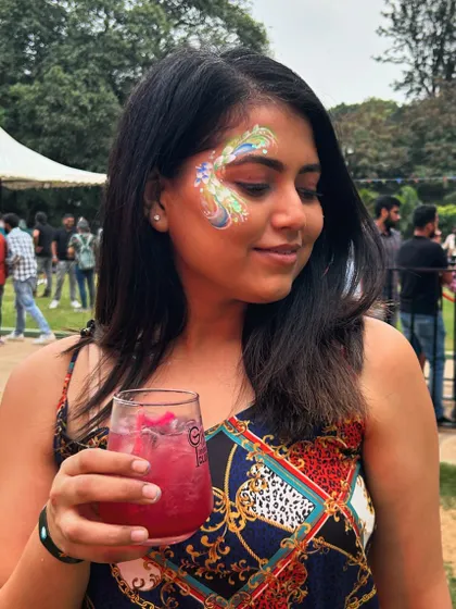 A client enjoying a drink at an outdoor event with her elegant, swirling floral face paint.