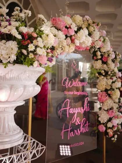 A beautiful acrylic welcome sign with elegant pink script, framed by a lush arch of pink and white flowers. This design is both modern and romantic, offering a personalized greeting to guests.