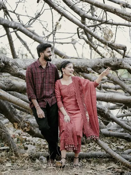 A couple in simple, elegant traditional outfits poses against a backdrop of fallen tree branches, blending nature with culture.