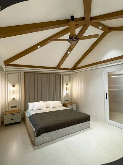 A sophisticated bedroom with a vaulted ceiling featuring exposed wooden beams. The neutral color palette and clean lines of the furniture create a calm and airy atmosphere.