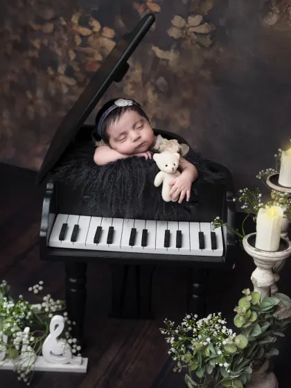 A truly artistic newborn portrait featuring a baby sleeping peacefully on a miniature grand piano. This elegant setup creates a stunning and unique piece of art.