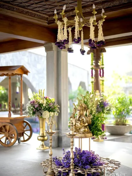 A Ganesha idol on a brass lamp stand, surrounded by fresh flowers at the entrance.