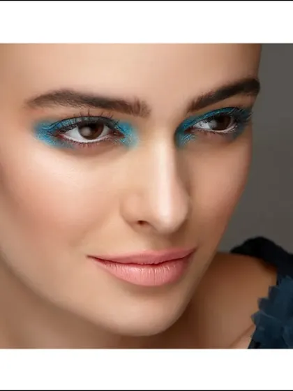 An editorial beauty shot with a pop of bright blue eyeshadow. The focus is tight on the eyes, showcasing a bold makeup choice with clean, luminous skin.