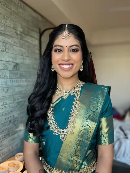 The bride's happy smile says it all. The makeup is fresh and radiant, complementing her beautiful teal saree and traditional jewelry.