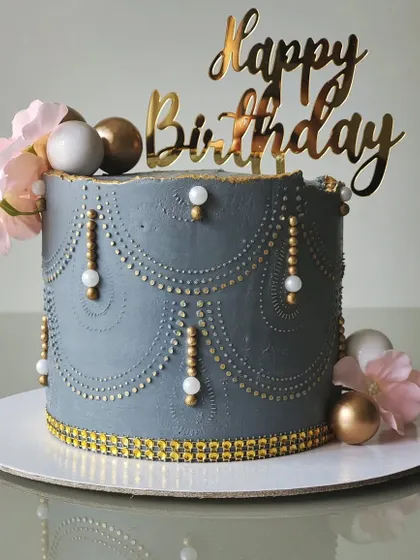 An elegant birthday cake in a dusty grey-blue, decorated with intricate, hand-piped drapery and pearl details. This design is a perfect example of how classic techniques can create a timeless and beautiful cake.