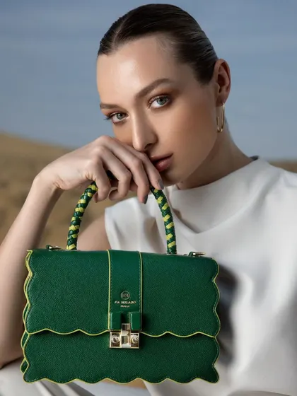 A close-up beauty and accessory shot for Da Milano. The styling is clean and minimal, with a simple white top and sleek hair, allowing the unique, scalloped-edge green handbag to be the hero of the image.
