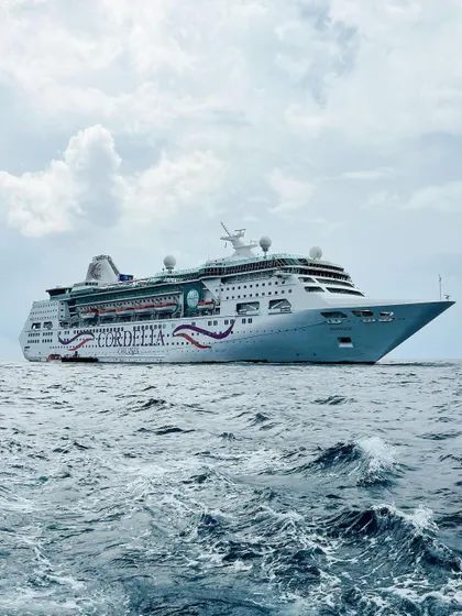 A dramatic shot of the Cordelia cruise ship on the open sea. The perspective emphasizes the vessel's size and the vastness of the ocean, creating a sense of adventure and escape.