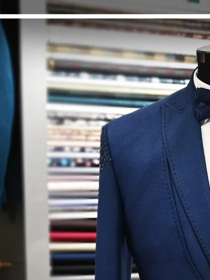 A close-up shot of a blue tuxedo jacket, highlighting the texture of the fabric and the detailed stitching.