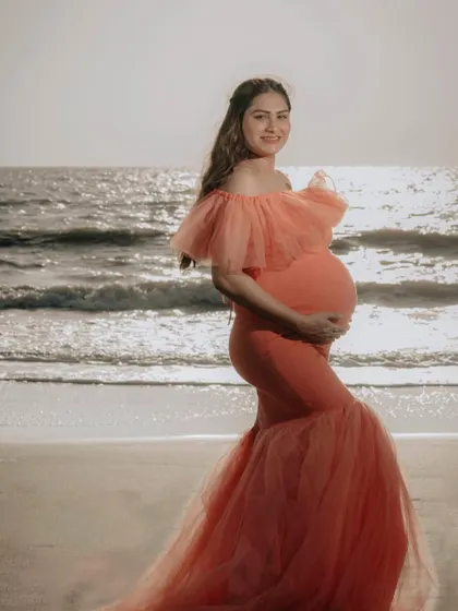 A sun-kissed shot of our peach off-shoulder mermaid gown on the beach. The warm light highlights the beautiful fit of the dress and the joy of the mom-to-be.