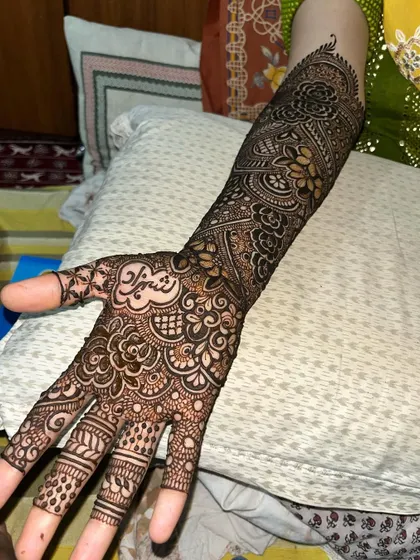 A single hand view of a bridal design, showing the name "Shehzad" on the palm surrounded by dense floral and paisley patterns.