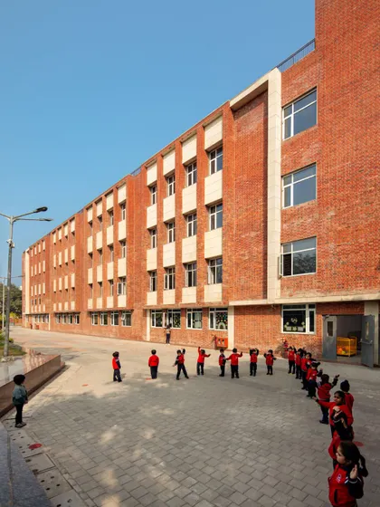 Students line up in the courtyard of HRM Global School, Delhi. The use of exposed brick and human-scaled design creates a warm and inviting atmosphere, making the school feel like a second home.