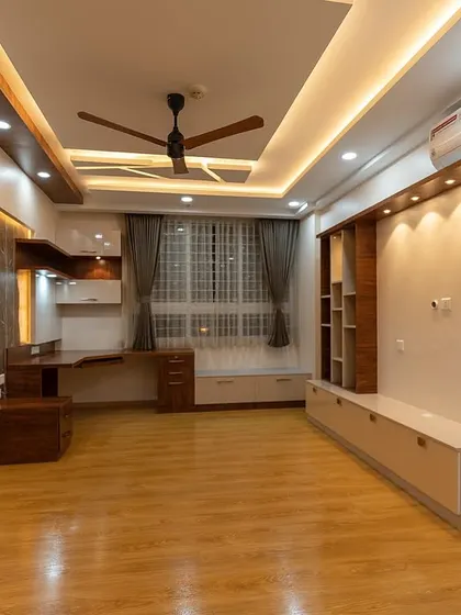 This spacious room combines a living area with a dedicated study nook. The design features a mix of wood tones and white finishes, complemented by layered ceiling lights, creating a multi-functional and cohesive living space.
