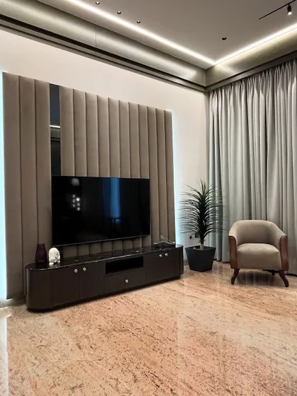 The TV and lounge area within the master bedroom. An upholstered, fluted wall panel creates a soft, luxurious backdrop for the television, with a comfortable armchair providing a perfect spot to relax.