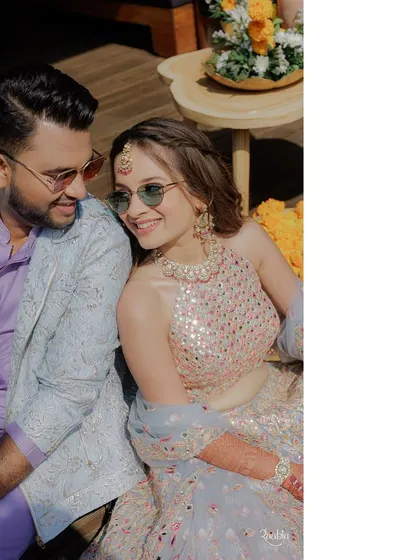 A happy, candid shot of the couple. The bride's subtle sunglasses add a cool, modern twist to her traditional-style lehenga, perfectly fitting the fun "carnival" theme.