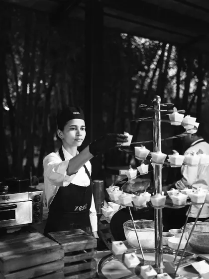 A black and white photo of a female chef carefully setting up a dessert tower.
