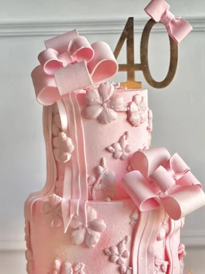 Pretty in pink and blooming with charm. This dreamy cake for a 40th birthday is adorned with delicate bows, floral textures, and a soft pink hue for a picture-perfect celebration.