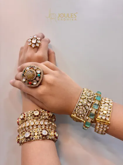 Two different styles of hand adornment. One hand features a stack of ruby kadas with a floral ring, while the other showcases emerald-accented bangles with a large Navratna-style ring.