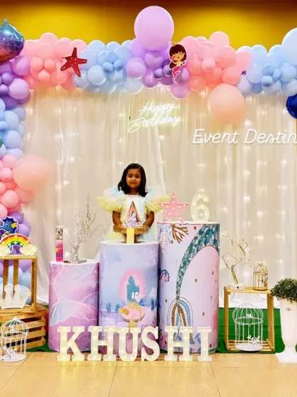 This mermaid-themed party decor creates a beautiful underwater scene. The setup includes a shimmering backdrop curtain, balloon tails, and themed pedestals, perfect for capturing photos.