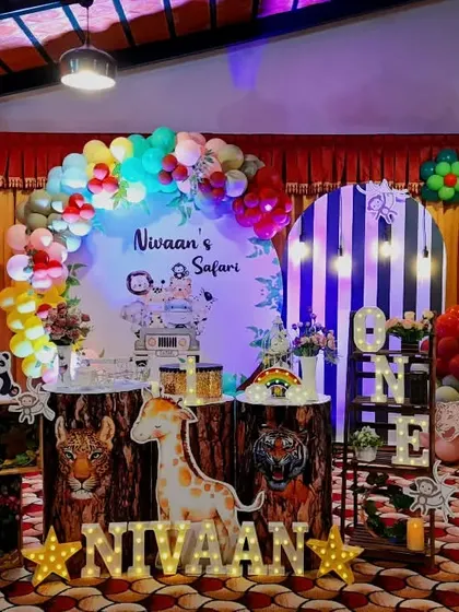 A grand safari setup for Nivaan's first birthday. This wide shot shows the full scale of the decor, with large animal props, log pedestals, and a multi-colored balloon arch.