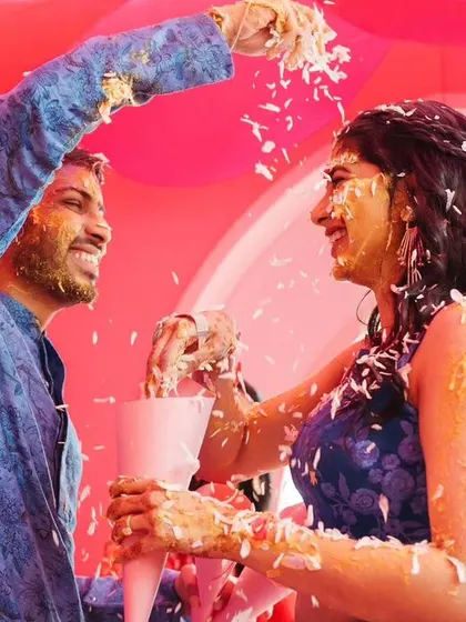 The couple playfully showering each other with rice and petals, a fun and candid moment from their 'Gulabi Haldi'.