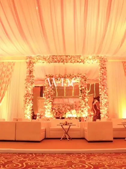 A lounge area at the Taj wedding, featuring a floral-framed photo booth and comfortable white sofas. The soft, warm lighting creates an inviting and elegant atmosphere.