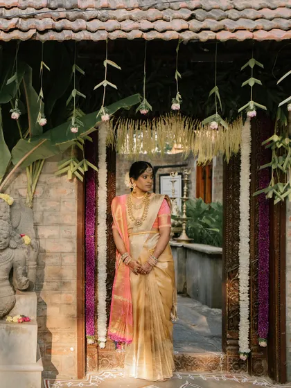 A stunning bride framed by a traditionally decorated doorway. We utilize the architectural beauty of heritage venues, enhancing them with simple floral garlands to create perfect photo opportunities.