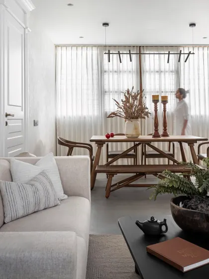 A shot of the combined living and dining space, highlighting the sheer curtains that diffuse natural light and the modern pendant light that defines the dining zone.