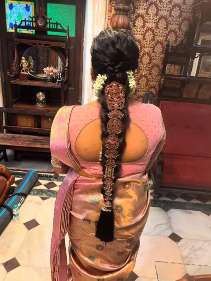 A traditional braid featuring antique finish temple jewellery. The look is softened with fresh white flowers at the base, blending classic adornment with natural elements.