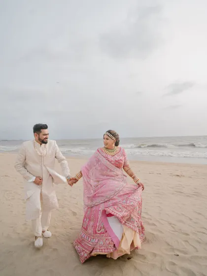 A happy stroll on the beach. This candid shot captures the couple's joy and the beautiful movement of the bride's lehenga against the ocean backdrop.