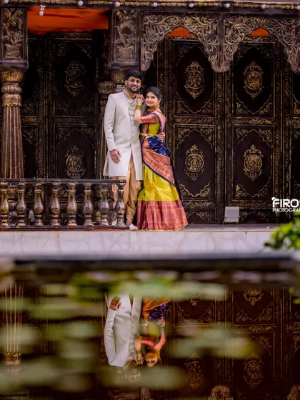 A beautiful reflection shot of a couple in traditional attire. The water perfectly mirrors their elegant outfits and the grand architecture.