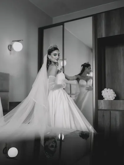 A bride in a beautiful white wedding gown looks at her reflection in a mirror, captured in a timeless black and white style. This image shows my approach to bridal photography, focusing on quiet, elegant moments.