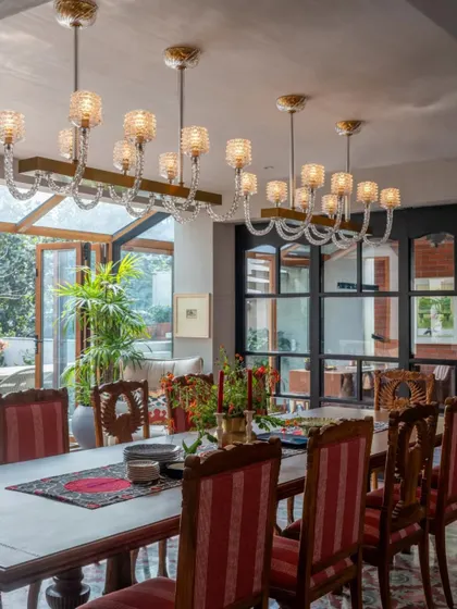 The dining area in the Dhaka residence is designed for large family gatherings. The long wooden table is surrounded by elegant chairs, and the space is illuminated by a series of beautiful glass chandeliers. The glass doors open to an outdoor patio, seamlessly blending indoor and outdoor living.