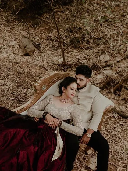A high-angle view of a couple relaxing on a vintage sofa placed in a rustic, wooded setting. This creative portrait blends elegance with nature.