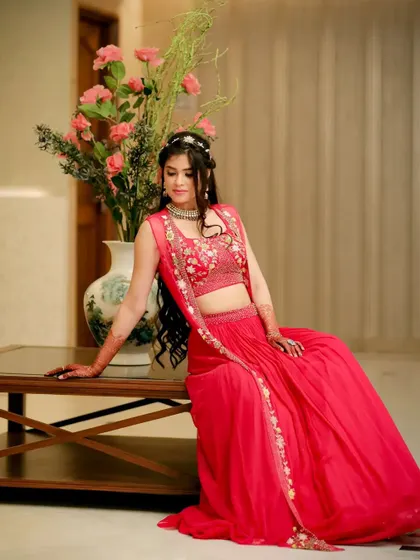 Sanya posing gracefully by a table with a flower vase, her red lehenga creating a beautiful pop of color.