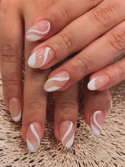 A duplicate of image 41, showing a chic and modern design on short, almond-shaped nails with a sheer nude base and bold white swirls.