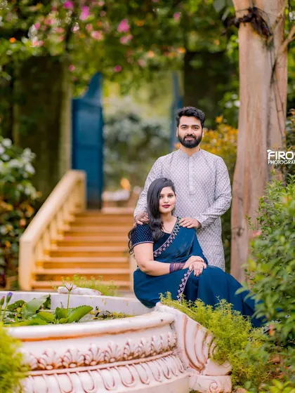 A serene and elegant portrait by a fountain. The couple's traditional outfits in shades of blue and white create a calm and sophisticated look against the garden backdrop.