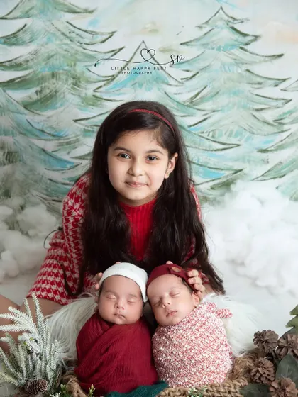A festive family portrait! This big sister is so proud to pose with her new twin siblings in a cozy Christmas-themed setup.