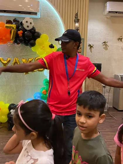 A head coach gives instructions to a group of children at a birthday party, with colorful balloons in the background. We combine celebration with structured, active fun.