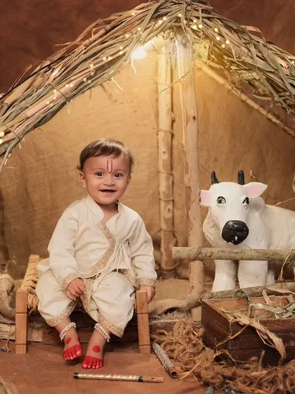 A happy little Krishna in our rustic village setup. The warm lighting and traditional props like the charpai and peacock create an authentic feel.