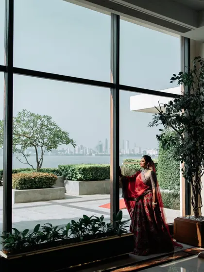 A bride in her stunning red lehenga, looking out a large window at the city skyline. This portrait combines her elegance with the grandeur of the urban landscape.
