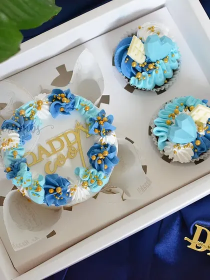 A Father's Day gift box featuring a mini cake and matching cupcakes. The blue and white theme with gold toppers makes for a very classy gift for dad.