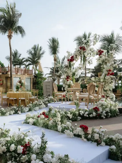 Set against the serene backdrop of the sea, this wedding ceremony arch is a picture of timeless romance. I wove together a tapestry of lush white hydrangeas and roses, punctuated with deep red blooms for a touch of passion. The design frames the couple and the ocean, creating a breathtaking setting for their happily ever after.