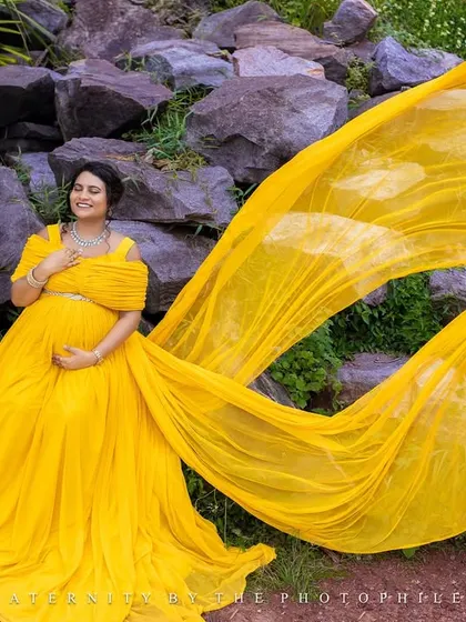 The long trail of the yellow gown creates a stunning visual as it cascades over the rocks in this outdoor nature setting.