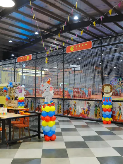 A wide view of the dining and play area decorated for a carnival party. Themed balloon columns with elephant and lion characters add to the fun.